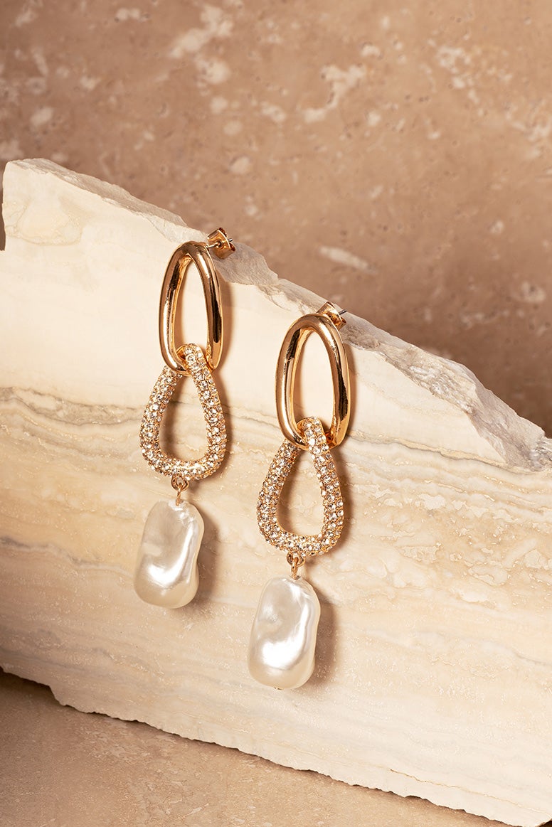 gold and pearl long drop earrings placed on a piece of marble like stone 