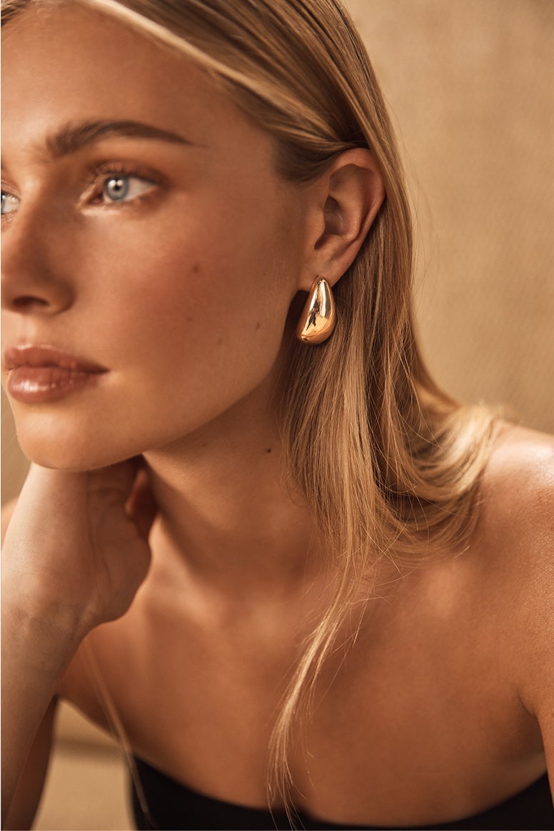 model with blonde hair tucked behind one ear wears a gold rounded organic shape bulbous stud earring 