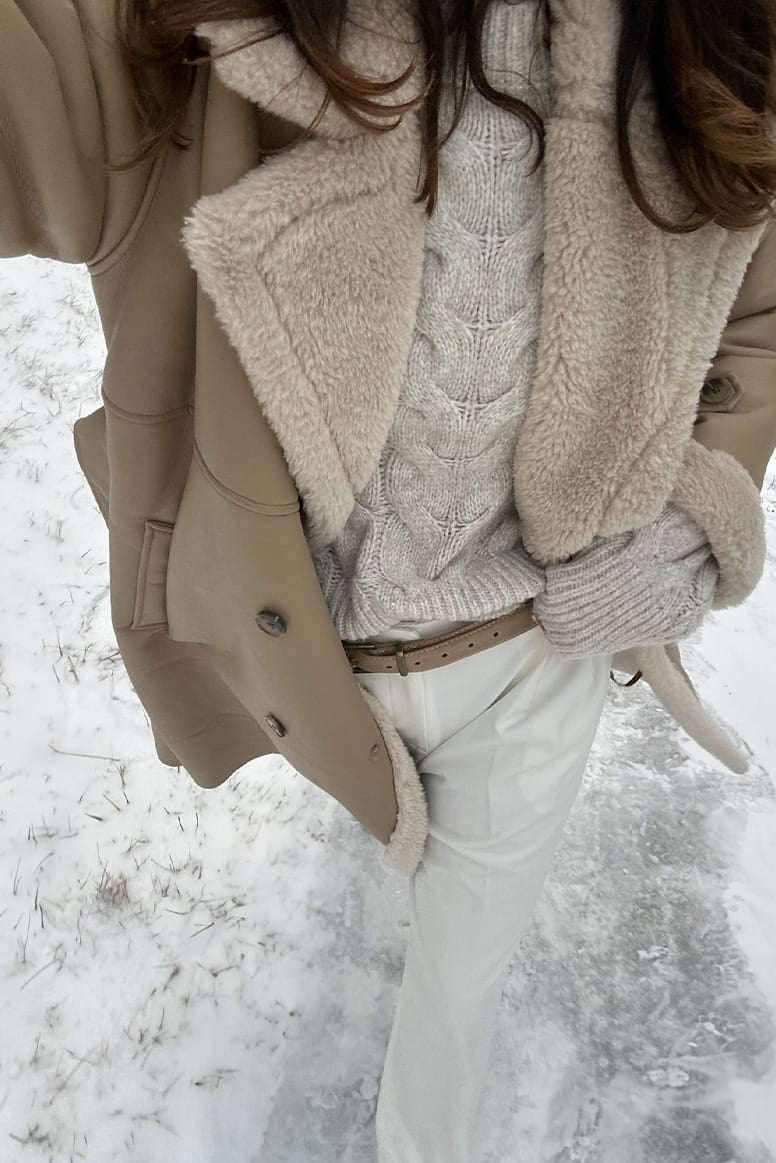 selfie style outfit photo where you cant see eloise mumme's head, the photo is more focused on the torso and legs, you can see shearling coat jumper and white pants with a camel coloured skinny belt