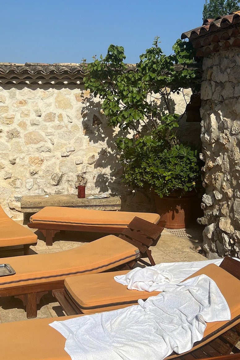 photo of several sun loungers with burnt orange cushions in front of a stone wall and a dark green tree