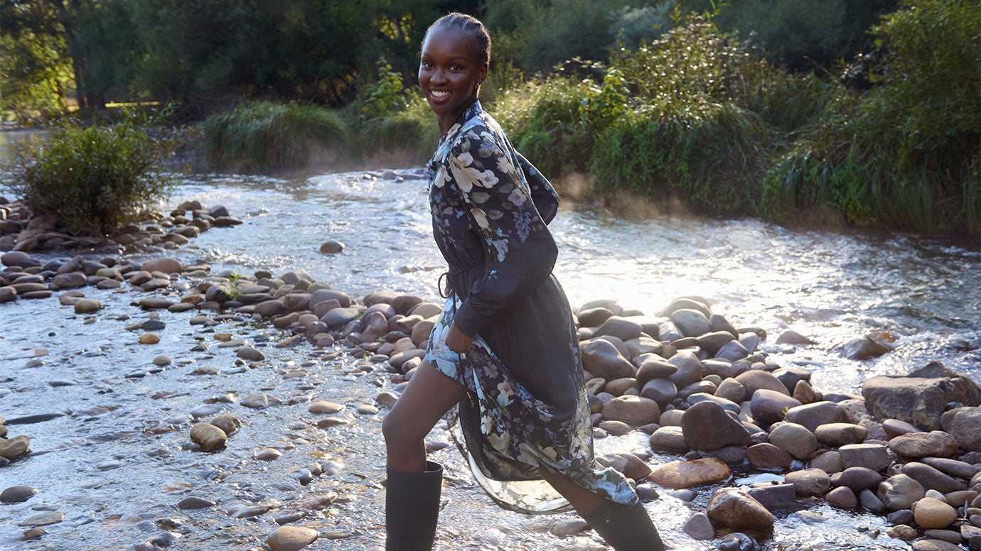 Model wears long dark floral dress styled with gumboots for a chic autumn/winter cold weather look.