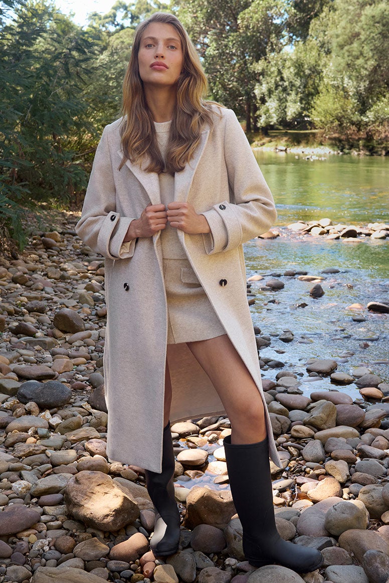 Model wears a matching co-ord set in neutrals styled with a long winter coat and gumboots for a chic wet-weather look.
