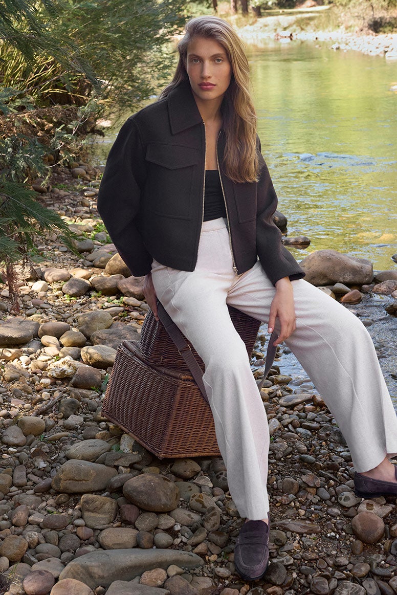 Model sits in comofrtable wide-leg white pants and black top, styles with a navy zip-through jacket with collar.