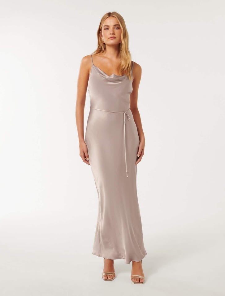model wearing a spaghetti slip dress with a flattering cowl neck and a simple waist tie, she has long blonde hair and is wearing strappy gold heels